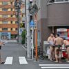 A sumo wrestler crosses the street as others buy drinks following a training session, near the Arashio-beya sumo stable in Tokyo